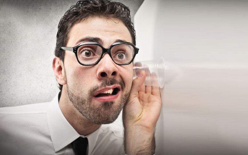 Man using a cup to listen through wall