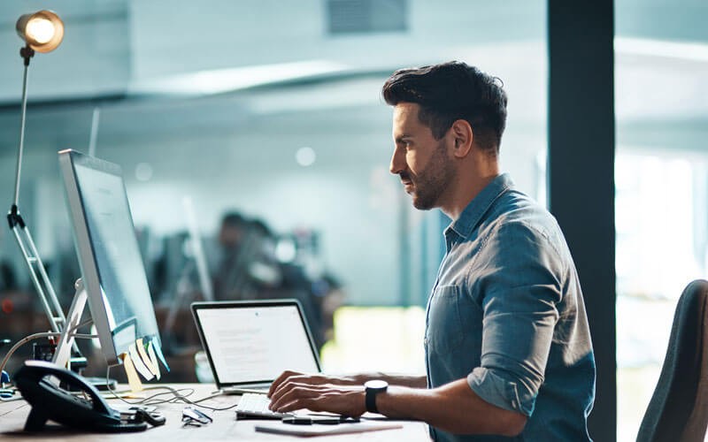IT professional with desktop and laptop computer working in office at night
