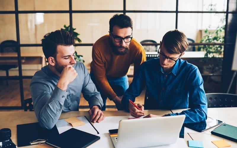 Group of casually dressed colleagues gathered around laptop in startup office