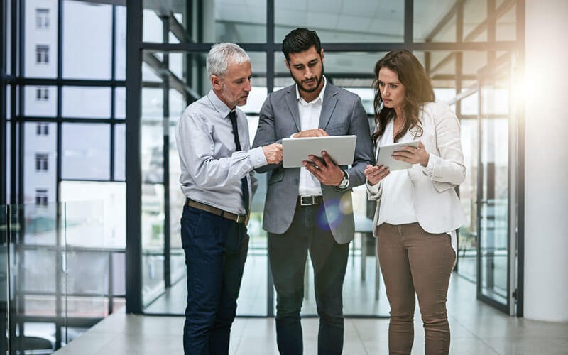 Group of business professionals standing around tablet device in hallway