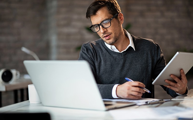 Optimise the cost and availability of cloud-based licenses Man holding a tablet while looking at a laptop
